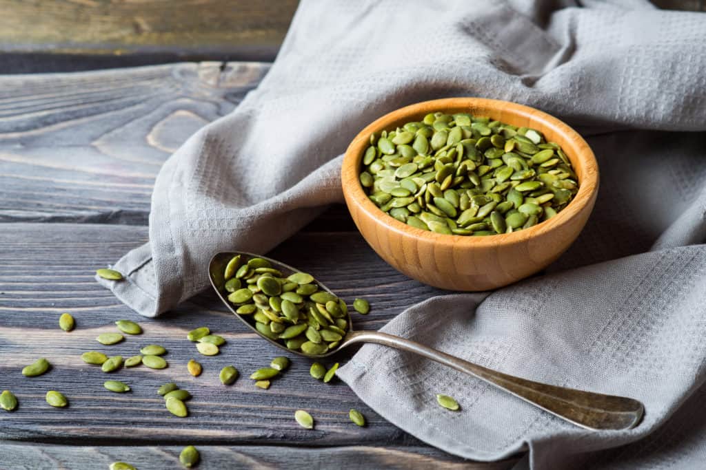 Raw Organic Pumpkin Seeds in vintage metal spoon over wooden background