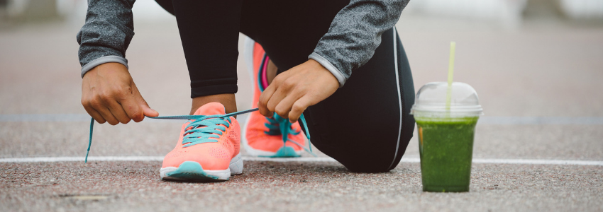 Runner tying shoes with green smoothie