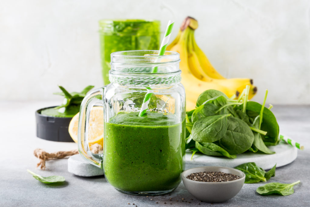 Batido verde saudável com as sementes dos espinafres, da banana, do limão, da maçã e do chia no frasco de vidro e nos ingredientes. Desintoxicação, dieta saudável, conceito de comida vegetariana.