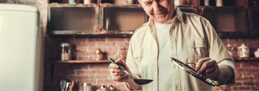 Handsome senior man is smiling while cooking in kitchen